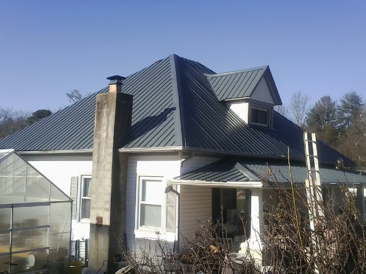 Dark blue standing seam metal roof on a white farmhouse with dormer — Slate & Tile Roof Repair by Roofing Brothers in La Rue