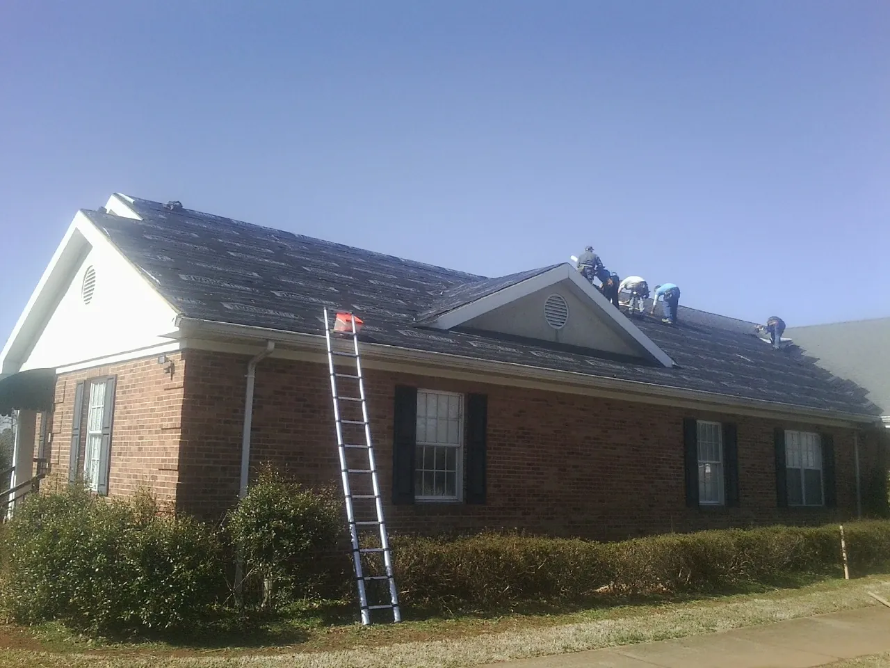 Crew tearing shingles off a brick ranch roof with a ladder set — Emergency Roof Repair work by our crew in La Rue