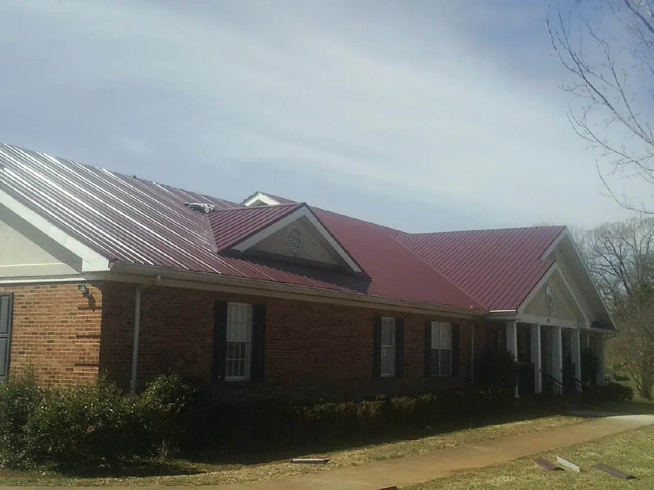 Red metal roof with gabled entries on a long brick building, from a Hail Damage Roof Repair job in La Rue