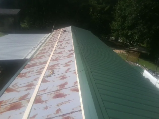 Old rusted panels beside newly installed green metal roofing — Wind Damage Roof Repair by Roofing Brothers in La Rue