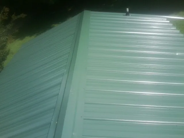New green metal panels meeting at the ridge of a roof — Flat Roof Repair work by our crew in La Rue