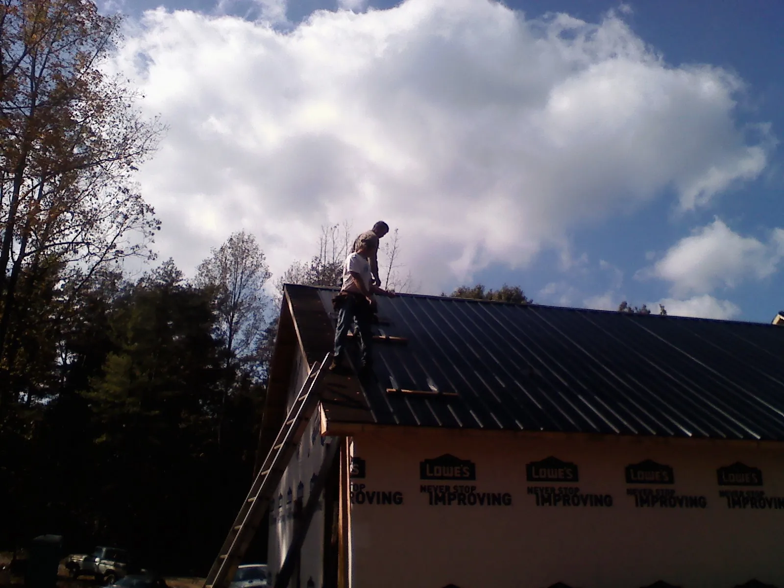 Roofer fastening dark metal panels high against a cloudy sky, from a Roof Inspection job in La Rue