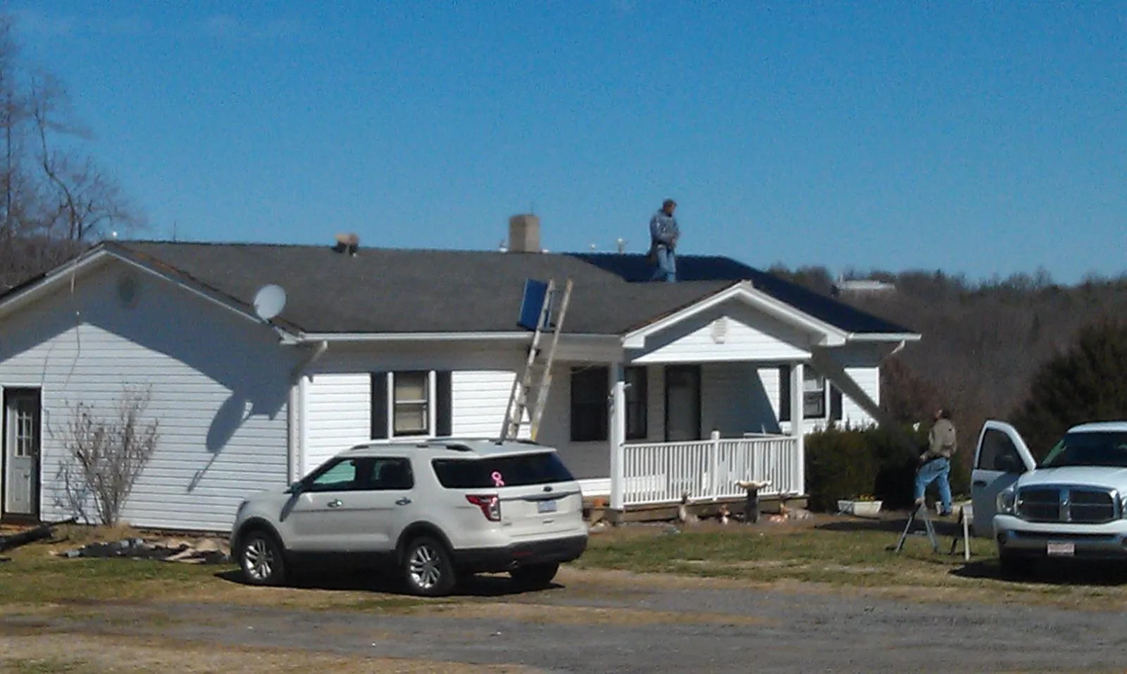 Roofers stripping shingles from a white ranch house roof in La Rue