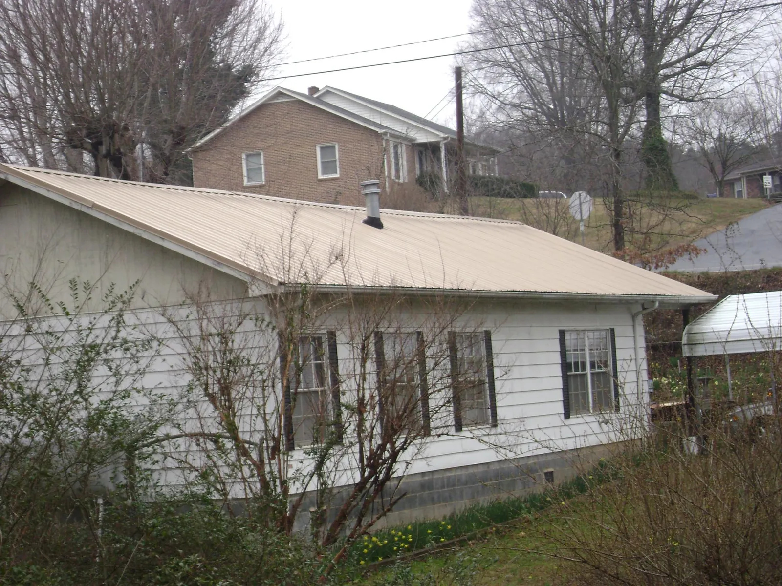 Tan metal roof on a white sided house set into a hillside — Commercial Roofing by Roofing Brothers in La Rue