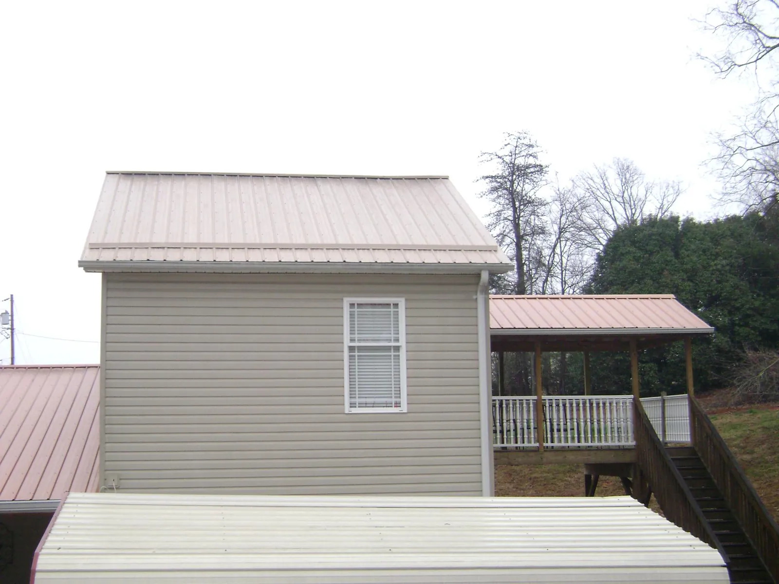Tan metal roofs on a two story addition and attached porch, from a Roof Replacement job in La Rue